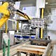 The ZEISS inline measuring station is completely automated: a robotic arm grabs the incoming cylinder head cover, holds it up to a blower to remove any residual metal chips, and clamps the cover on the loading table.