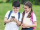 happy schoolchildren using smartphone outdoors together