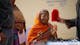 Indian woman with glasses looks into mirror.