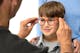 Een oogarts plaatst een nieuwe bril op het gezicht van een jongetje om te zien of hij goed past.
